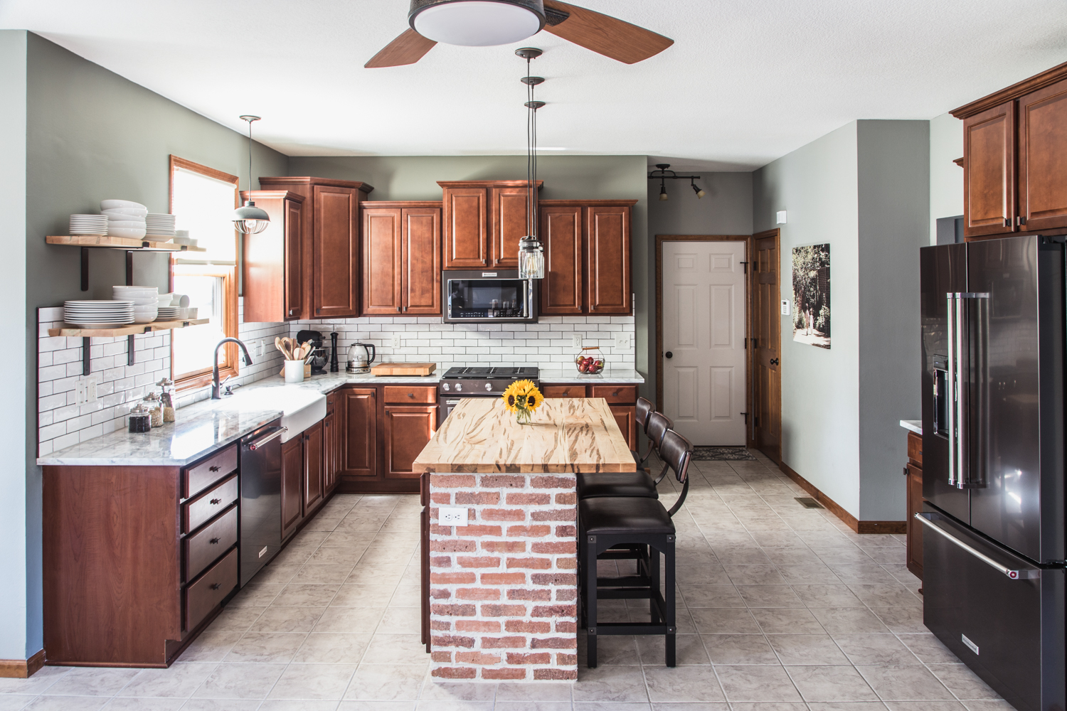 kitchen with dark cabinets, white subway tile, black stainless appliances, exposed brick, wood countertop, island, quartzite countertop