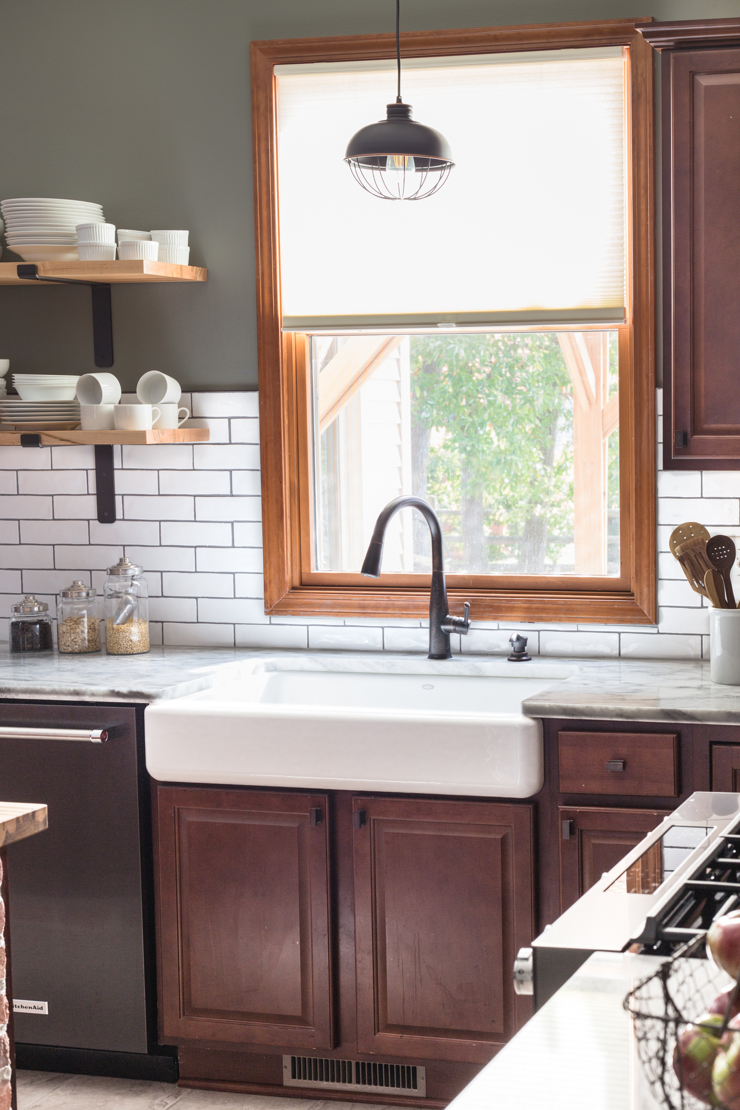 white farmhouse sink with dark cabinets, bronze faucet, white subway tile, and black stainless dishwasher